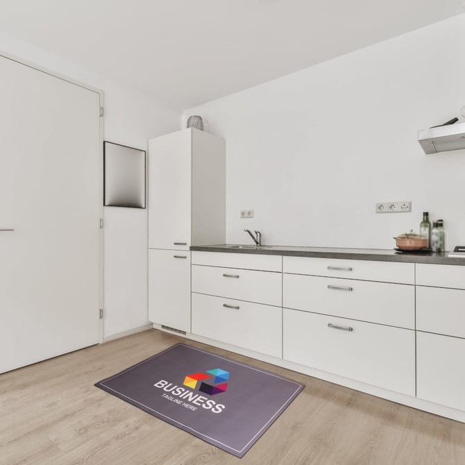 A rectangular diatomite mat in grey with a logo, placed on a wooden kitchen floor.