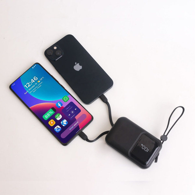 A black portable power bank connected to a smartphone, both displaying charging indicators. The power bank has a logo.