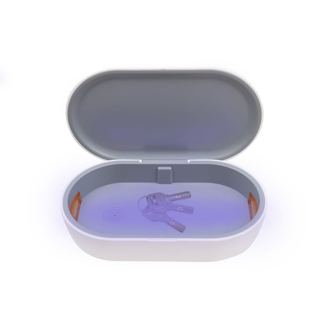 A white UV sterilisation box with a grey interior, containing keys and showcasing a wireless charging feature.