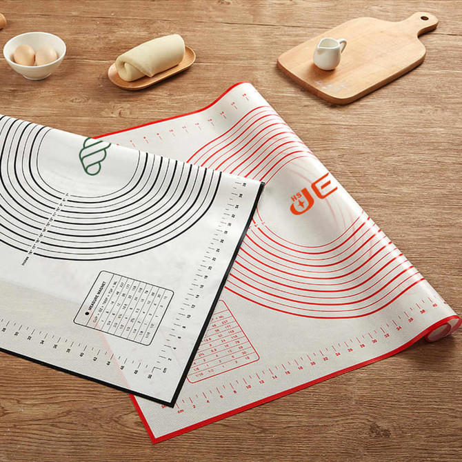 A silicone pastry mat in white and black features measurement markings and a logo, placed on a wooden surface.