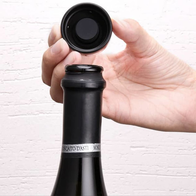 A drink bottle with a black neck, featuring a black champagne bottle stopper being placed on top.