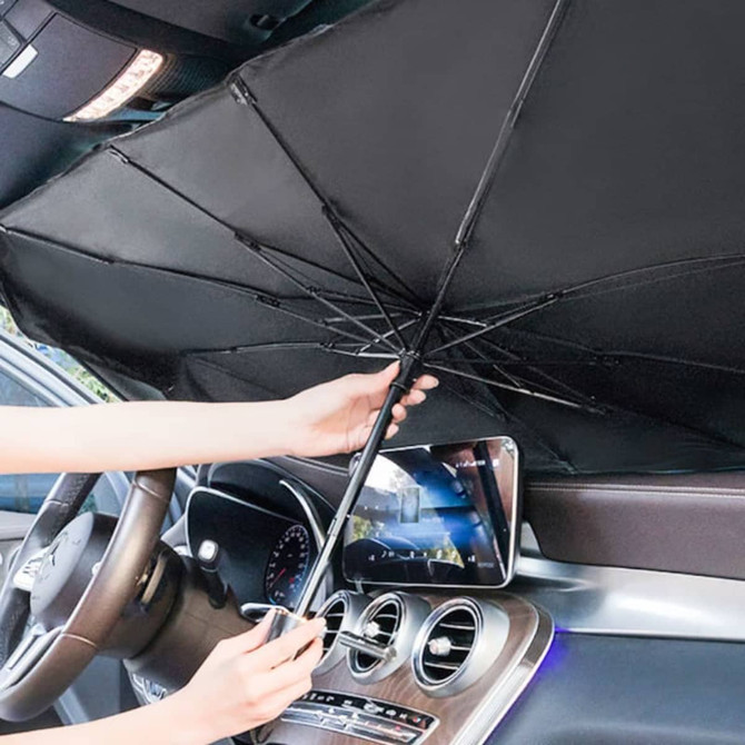 A black car shade umbrella being held inside a vehicle, with a smartphone visible in the background.