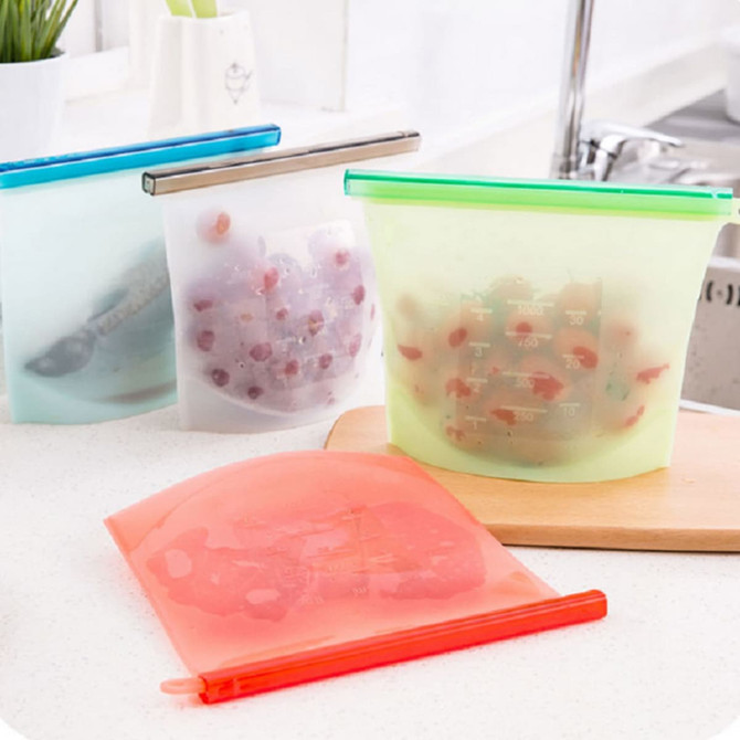 Silicone reusable storage pouches in various colours, featuring a sealing mechanism and measuring marks, arranged on a countertop.