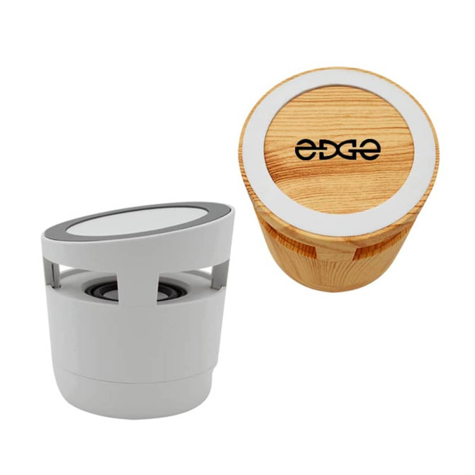 A two-tone Bluetooth speaker in white and wood finish with a wireless charging surface and a logo on top.