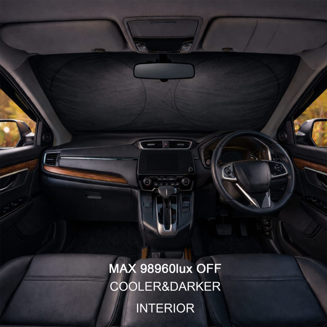 A car interior featuring a black reflective sunshade across the windshield, with leather seats and wooden accents.