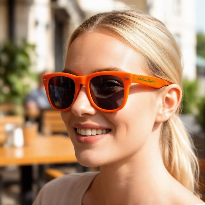 A pair of vibrant orange folding sunglasses with dark lenses, displayed on a smiling woman outdoors.