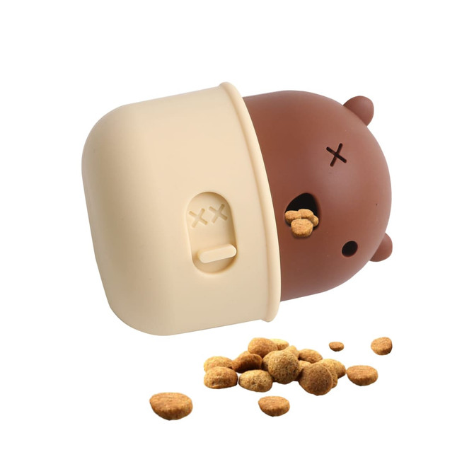 A brown and cream dog treat dispenser toy, shaped like a bear, with kibble scattered around it.