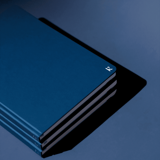 A navy blue hardcover notebook with a subtle logo, featuring multiple stacked layers on a dark background.