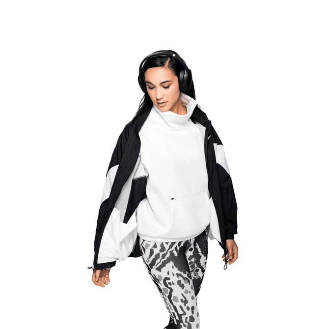 A woman wearing a black and white jacket and patterned leggings, listening to headphones. The product features a logo.