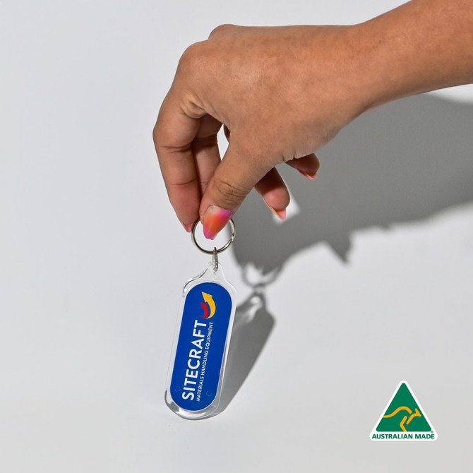 An oval acrylic keychain in blue, held by a hand, featuring a logo and an Australian Made badge.