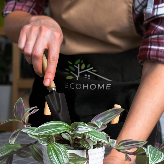 A person using a black trowel with a wooden handle, wearing an apron with a logo, tending to a potted plant.