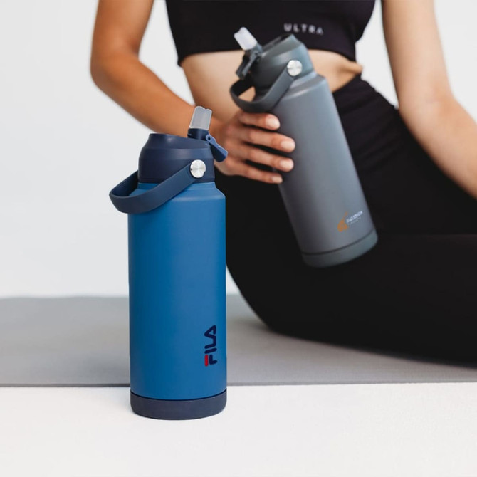 A drink bottle in navy blue with a handle and lid, featuring a logo, alongside a grey bottle in use.