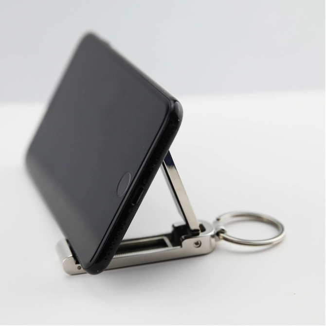 A black phone propped up by a silver mobile stand and hanger key ring, showcasing its compact design.