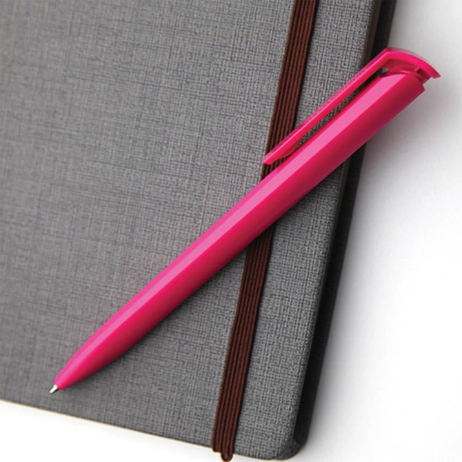 A pink plastic pen rests on a grey textured notebook, featuring a clip and smooth barrel design.
