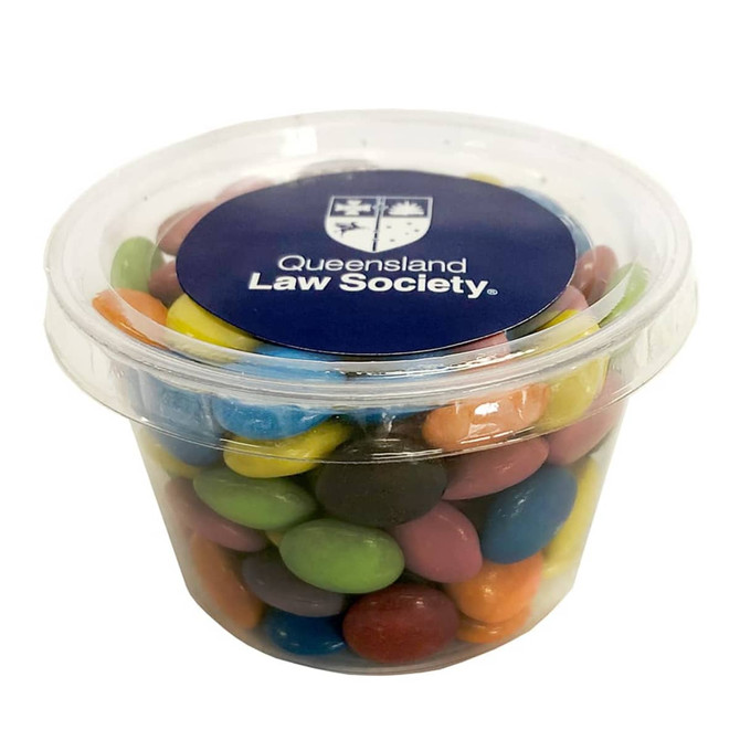 A clear tub filled with multicoloured choc beans, featuring a lid with a logo.