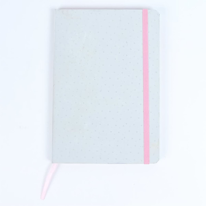 A grey notebook with a pink elastic band and a ribbon bookmark, featuring a dotted texture on the cover.