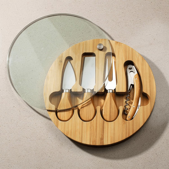 A round bamboo cheese board set featuring four stainless steel knives and a corkscrew, with a glass lid.