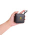 A portable black wireless Bluetooth speaker held in a hand, featuring a branded logo on the front.