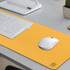 A yellow PU leather desk mat with a white mouse and keyboard on a grey desktop. Features a logo in the corner.