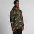 A man wearing a green and brown camouflage hoodie with a front pocket and drawstring hood, featuring a logo.