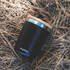 A drink bottle in matte black with a wooden lid, featuring a simple logo on the side, resting on straw.
