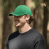 A green organic cotton twill cap worn by a man in a black t-shirt, set against a natural background.