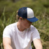 A navy and white trucker cap with a mesh back, worn by a person sitting outdoors in casual clothing.