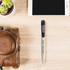 A wheat straw click pen in grey with a black grip, placed beside a smartphone and a brown leather bag.