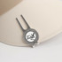 A silver golf divot tool with a ball marker attached, resting on a beige cap. It features a logo design.