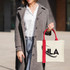 A woman holds a cream-coloured horizontal canvas tote bag with red handles, featuring a logo.