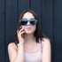 A drink bottle opener integrated into blue sunglasses, worn by a woman against a dark wooden background.