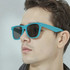A pair of turquoise sunglasses with dark lenses, displayed on a model's face. The sunglasses feature a branding logo.