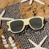 Glow in the dark sunglasses in pale yellow, resting on a patterned beach mat with seashells and starfish.