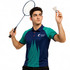 A young man in a blue and green polo shirt holds a badminton racket and shuttlecock, featuring a logo.