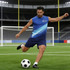 A man in a blue sleeveless micro mesh singlet kicks a soccer ball on a field, with goals in the background.