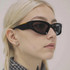A pair of black wraparound sunglasses with dark lenses, worn by a person with light blonde hair.