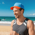 A man wearing a blue and orange Sandwich Bill Hat smiles at the beach, with waves and surfers in the background.