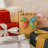 A collection of wrapped gifts in various colours, featuring a brown paper bag with a rainbow satin ribbon.