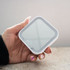 A compact mirror with LED light in a square, white casing held in a hand.