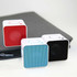 Three square Bluetooth speakers in red, blue, and black, resting on a dark grey surface.