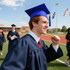 A blue mortarboard graduation cap worn by a smiling graduate in a navy gown on a sports field.