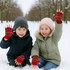 Fingerless gloves in red with patterned designs, worn by two children in winter attire, playing in the snow.