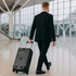 A black hardside suitcase on wheels is being pulled by a man in a suit in an airport terminal.