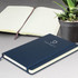 A large, navy blue Moleskine notebook with an elastic closure, featuring lined pages. A potted plant is in the background.