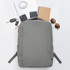 A grey backpack surrounded by a notebook, sunglasses, keys, phones, and a charger on a white background.
