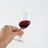 A glass wine glass held in a hand, filled with deep red wine, featuring a clear glass design and a sturdy base.