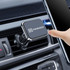 A car hook bracket in black and silver, attached to an air vent, with a hand placing a smartphone nearby.