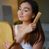 A beech wood comb in a person's hand, with long dark hair being styled in front of a mirror.