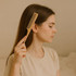A bamboo rat tail comb held by a woman with long hair, set against a neutral background.