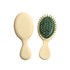A mini paddle brush with a cream handle and green bristle base, featuring a logo on the handle.